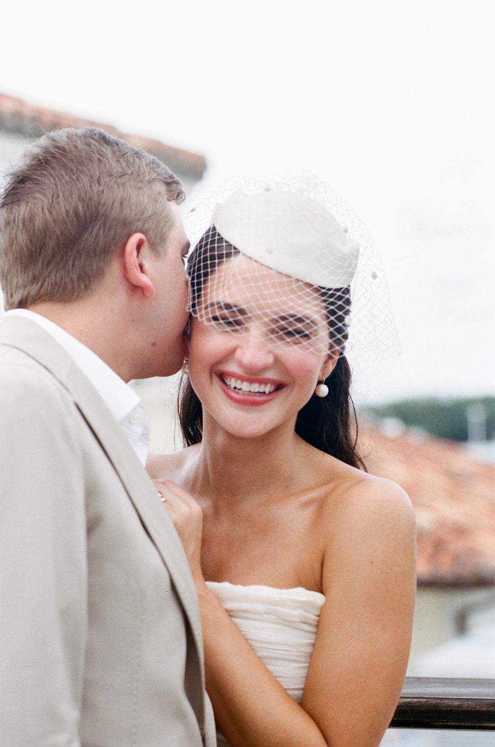 A romantic wedding moment captured outdoors with the couple sharing a sweet, intimate exchange against a blurred background.