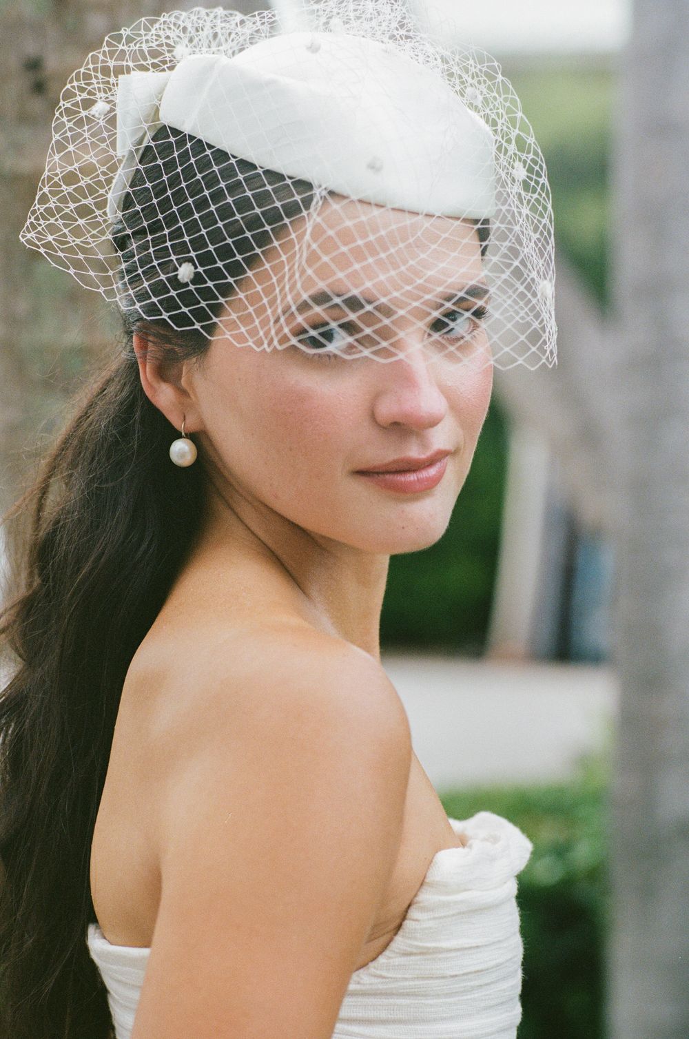 A bride wearing a classic white veil and strapless dress poses in an elegant outdoor portrait series.