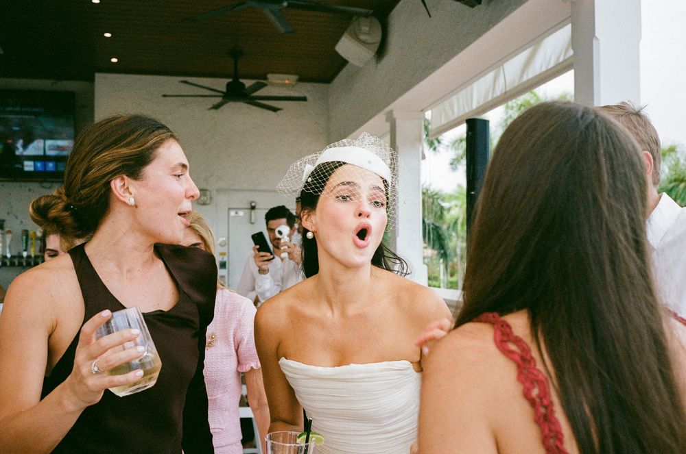 A candid moment at a wedding reception shows guests in casual and formal attire sharing laughter and drinks on a covered patio.
