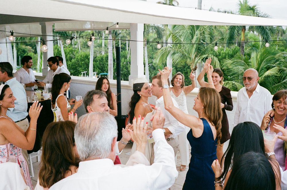 Wedding guests dance and celebrate together on a covered outdoor patio during a lively reception party.