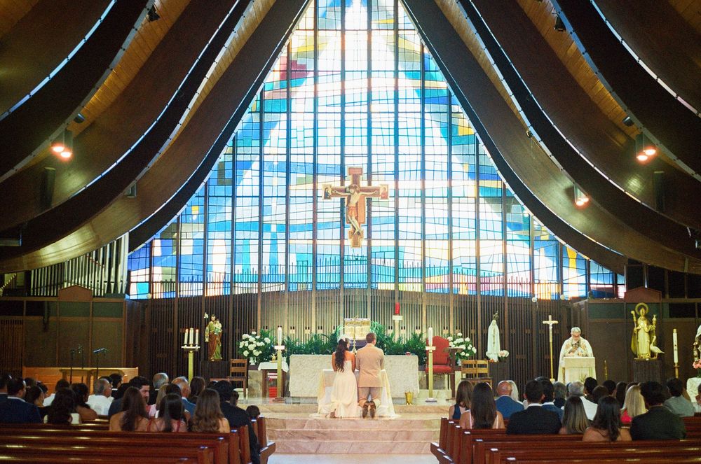 Interior view of a modern church with dramatic curved wooden beams and large stained glass windows.