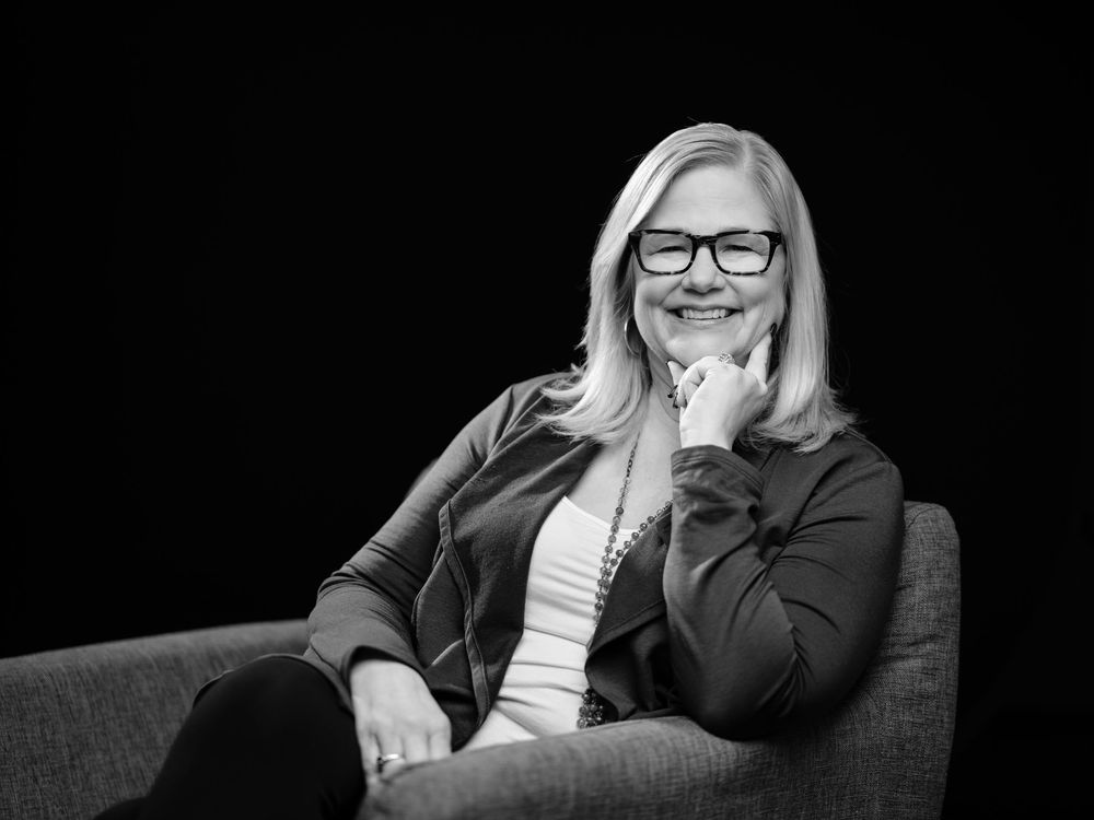 Professional black and white headshot photo of someone in business attire with glasses and blonde hair smiling at camera.