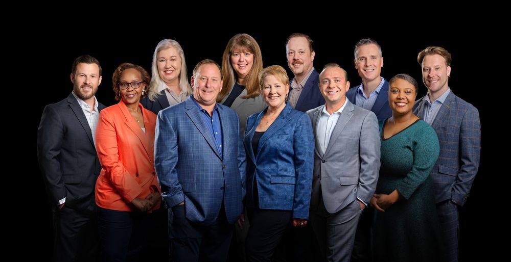 Professional business team in formal attire poses together against dark background for corporate portrait.