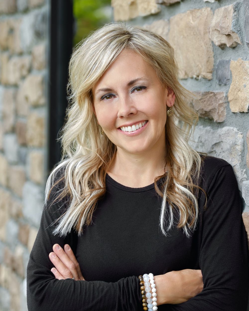 Professional headshot of someone in black sweater against stone wall background with warm lighting.