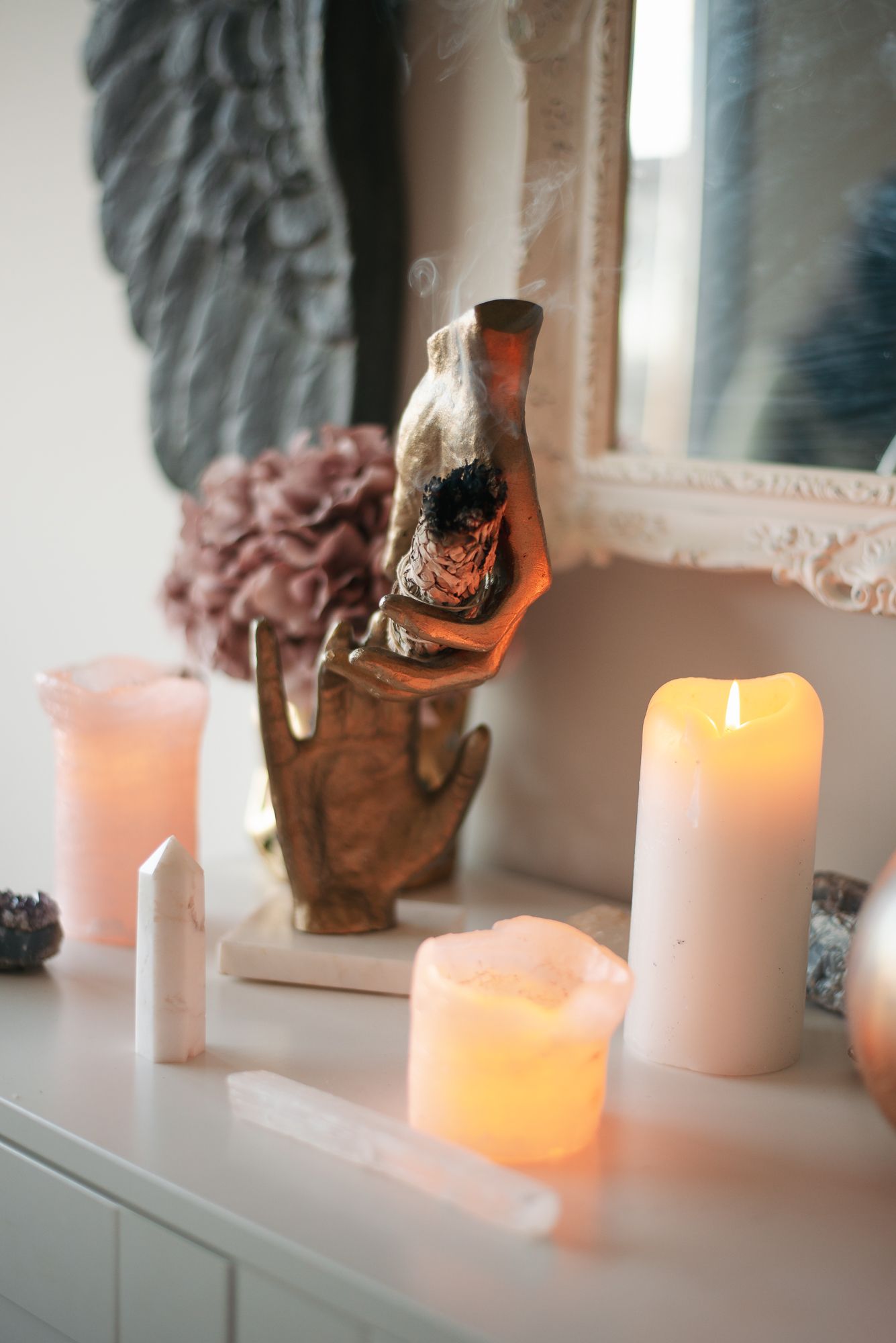 Glowing white candles and a decorative bottle create a cozy atmosphere on a white vanity with soft lighting.