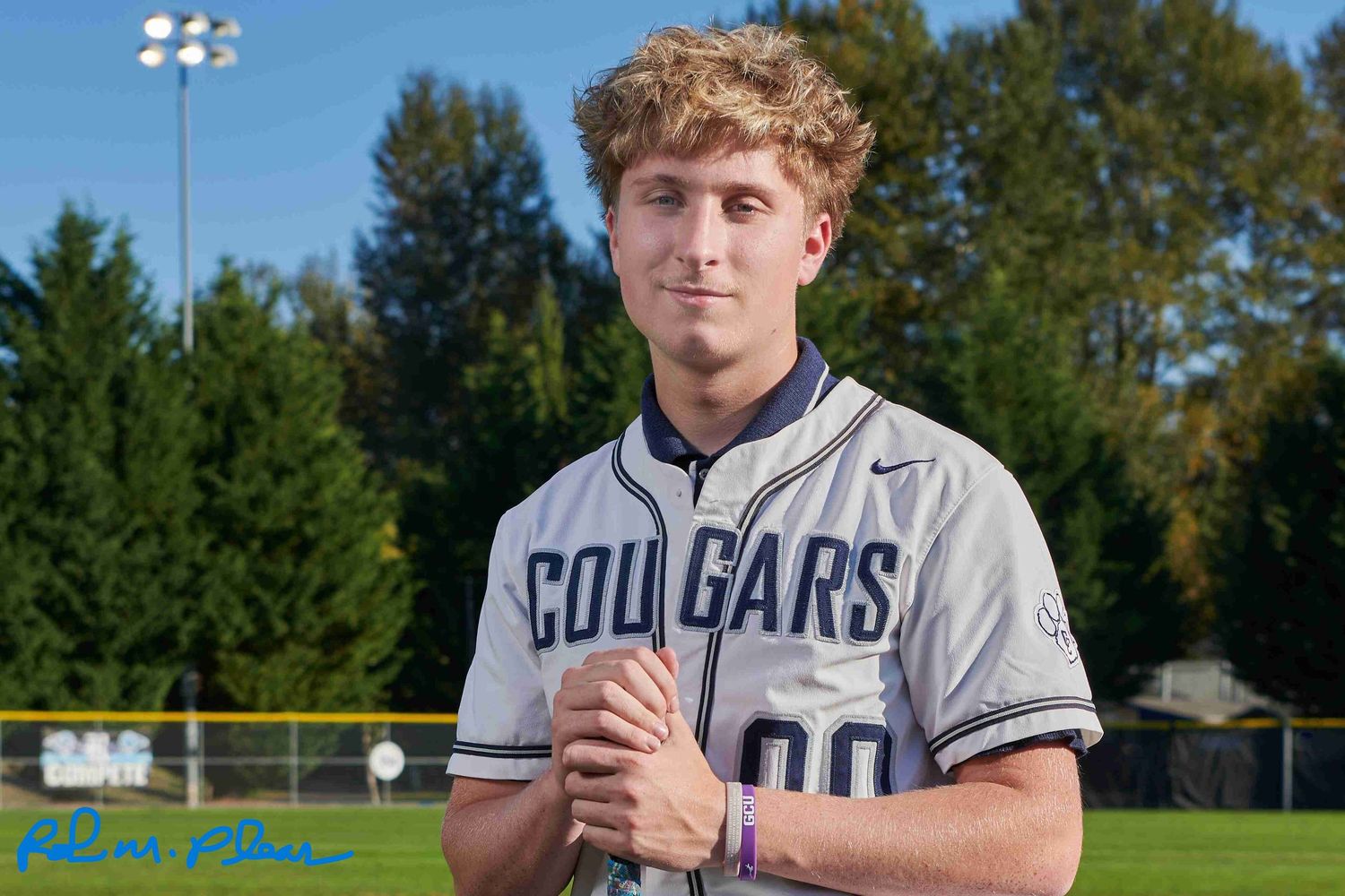 High school senior male at Heritage Recreation Center, Puyallup, kneeling on pitcher's mound on baseball field, holding baseball bat.