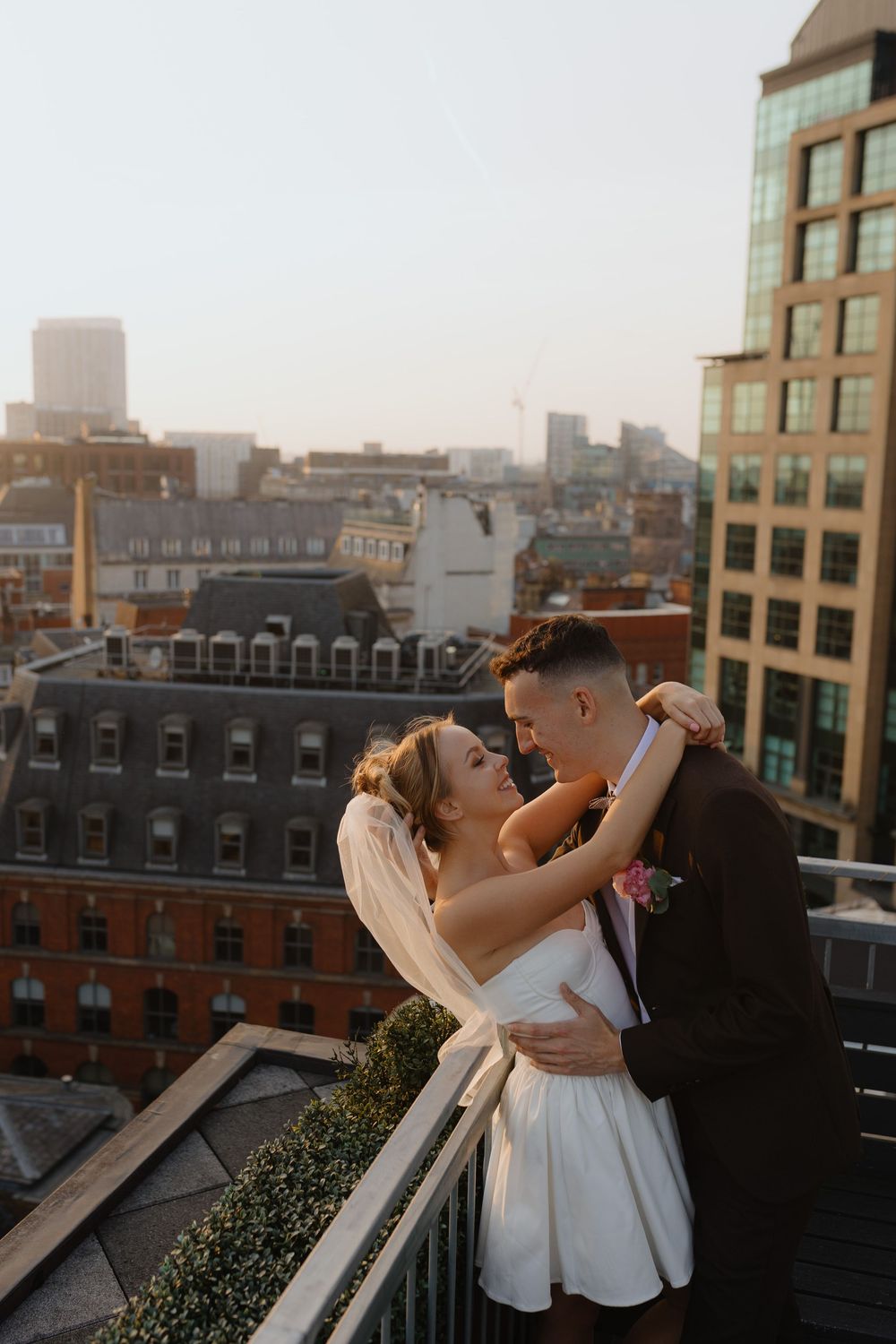 A couple shares an intimate dance moment on a rooftop with city buildings in the background at sunset.