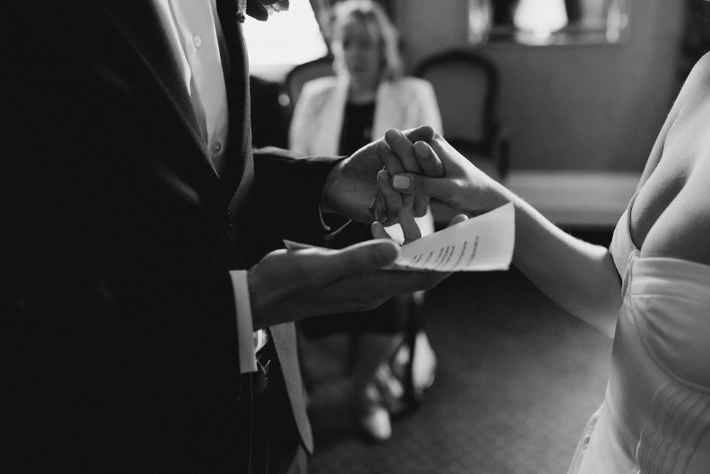 Black and white photo of a couple exchanging rings during an intimate wedding ceremony.