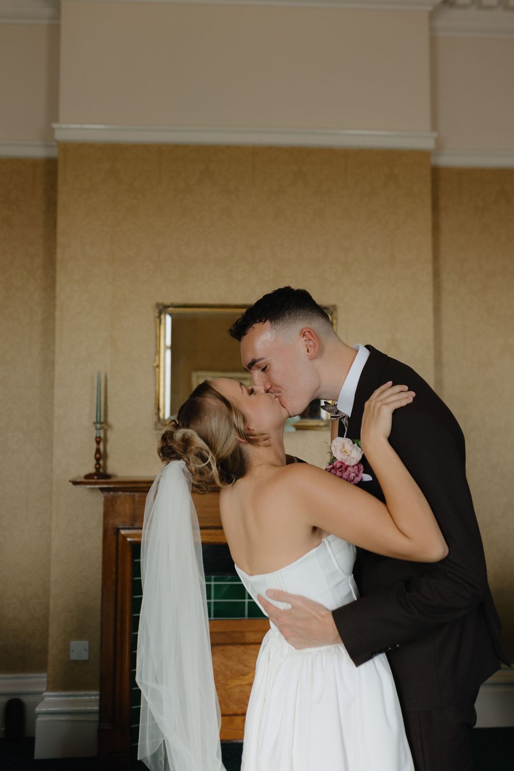 Romantic newlywed couple sharing their first kiss in an elegant room with warm lighting.