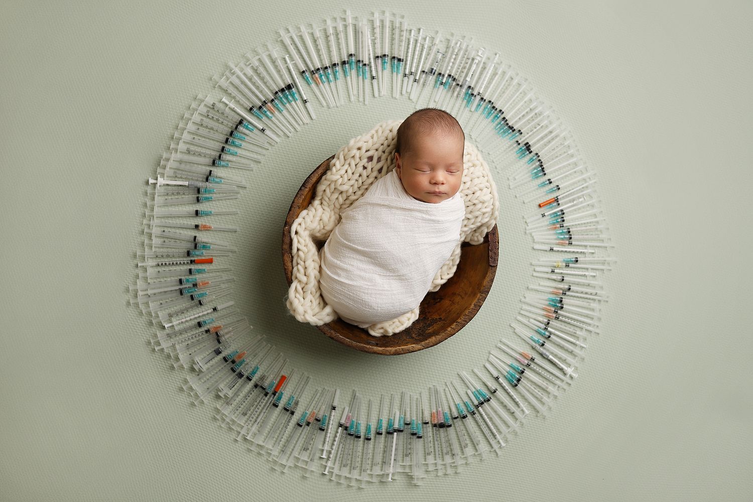 A newborn baby lies in a wooden bowl surrounded by a circular arrangement of blue and white clothespins. IVF newborn photography