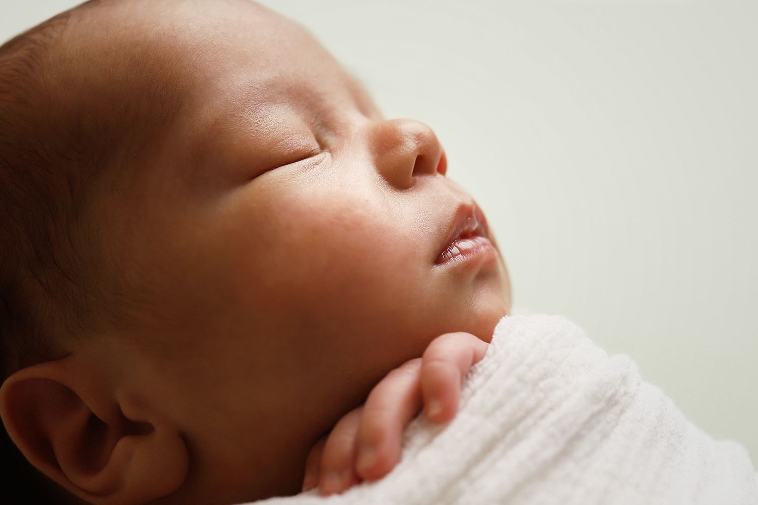 A close-up profile view of a sleeping newborn baby wrapped in white swaddling cloth. Utah newborn photography