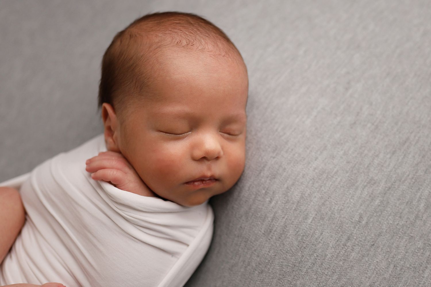 A sleeping newborn baby swaddled in light gray fabric is photographed from different angles in a collage. Utah newborn studio