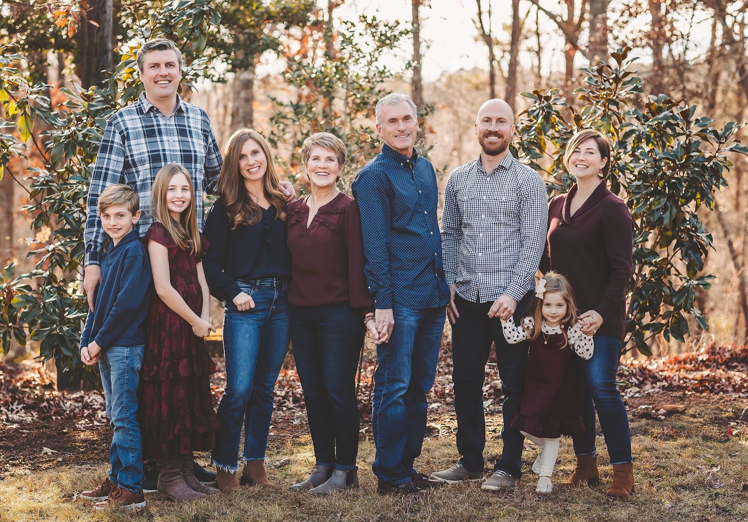 A group of people wearing casual clothing pose together outdoors among autumn trees during a family photo session.