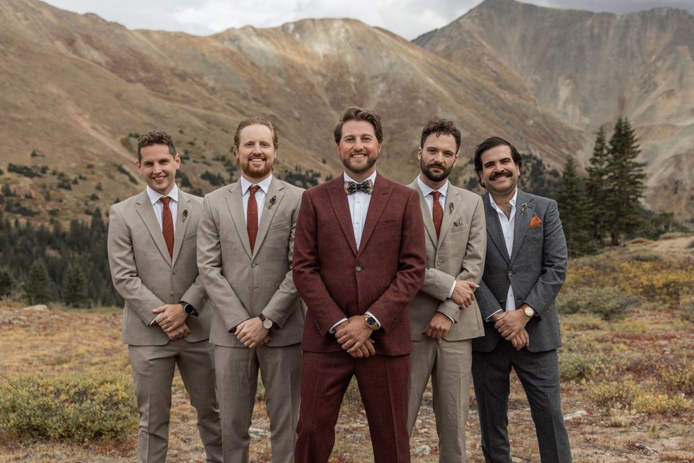 Wedding party in formal attire poses against scenic mountain backdrop in autumn setting.
