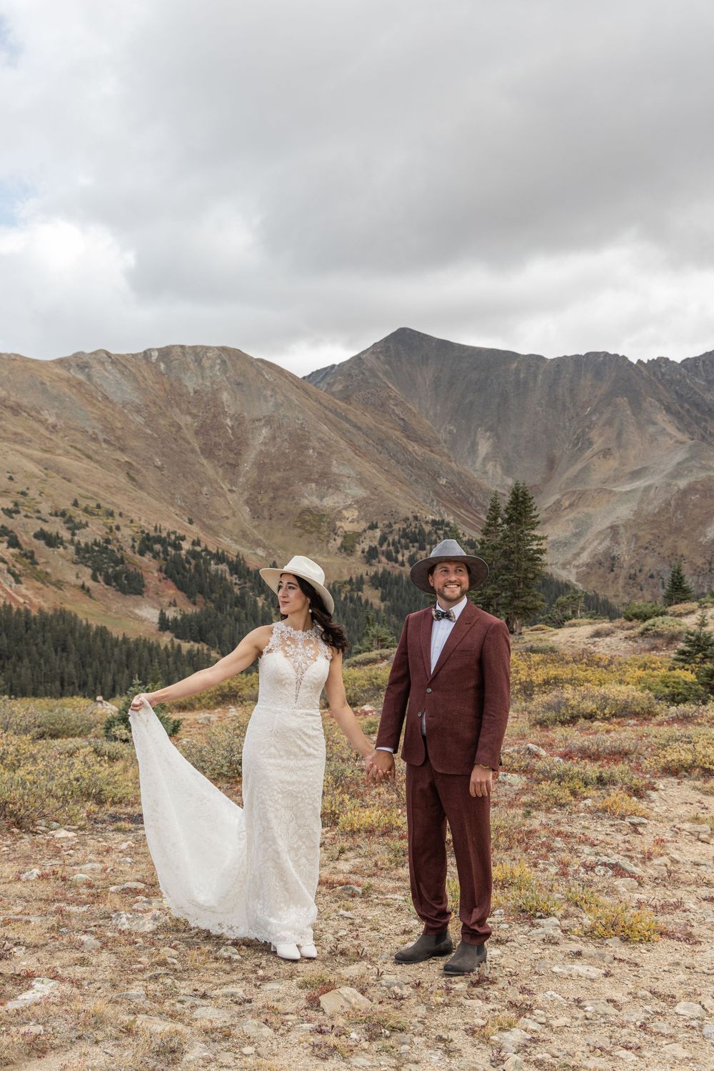 A couple poses in their wedding attire against a stunning backdrop of rugged mountain peaks and alpine meadows.