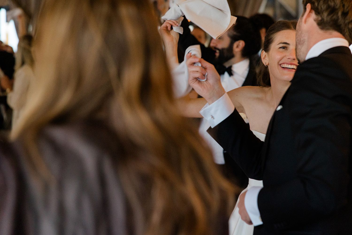 Wedding guests smile and watch the dance floor during an indoor reception celebration.