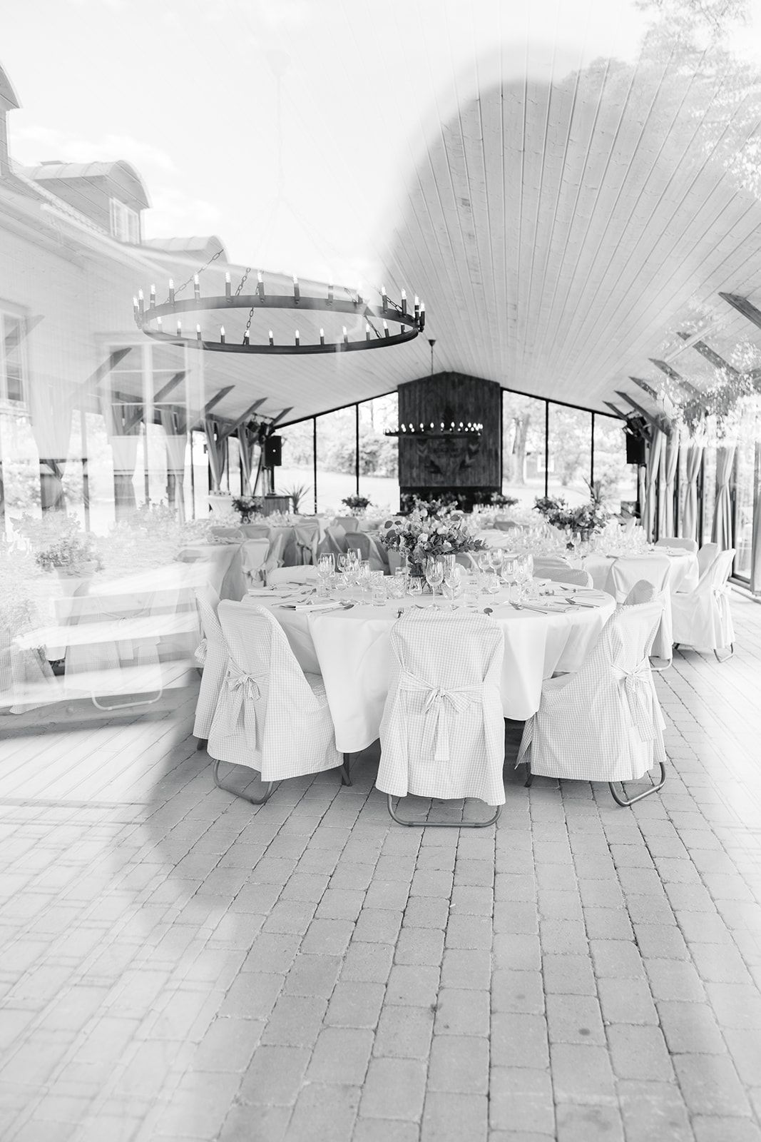 Black and white panoramic view of an elegant wedding reception venue with white-clothed tables and chairs arranged indoors.