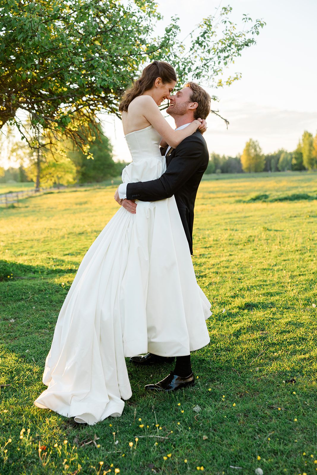 A romantic couple in wedding attire dances together in a sunlit meadow during golden hour.