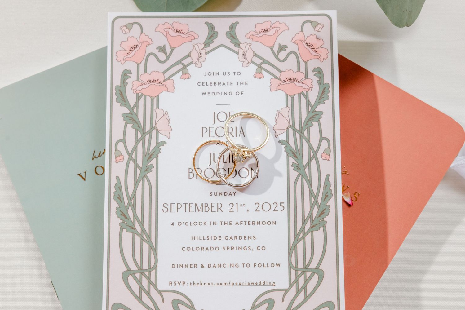 Art nouveau style wedding invitation with pink and sage green floral design and gold accents on colored envelopes.
