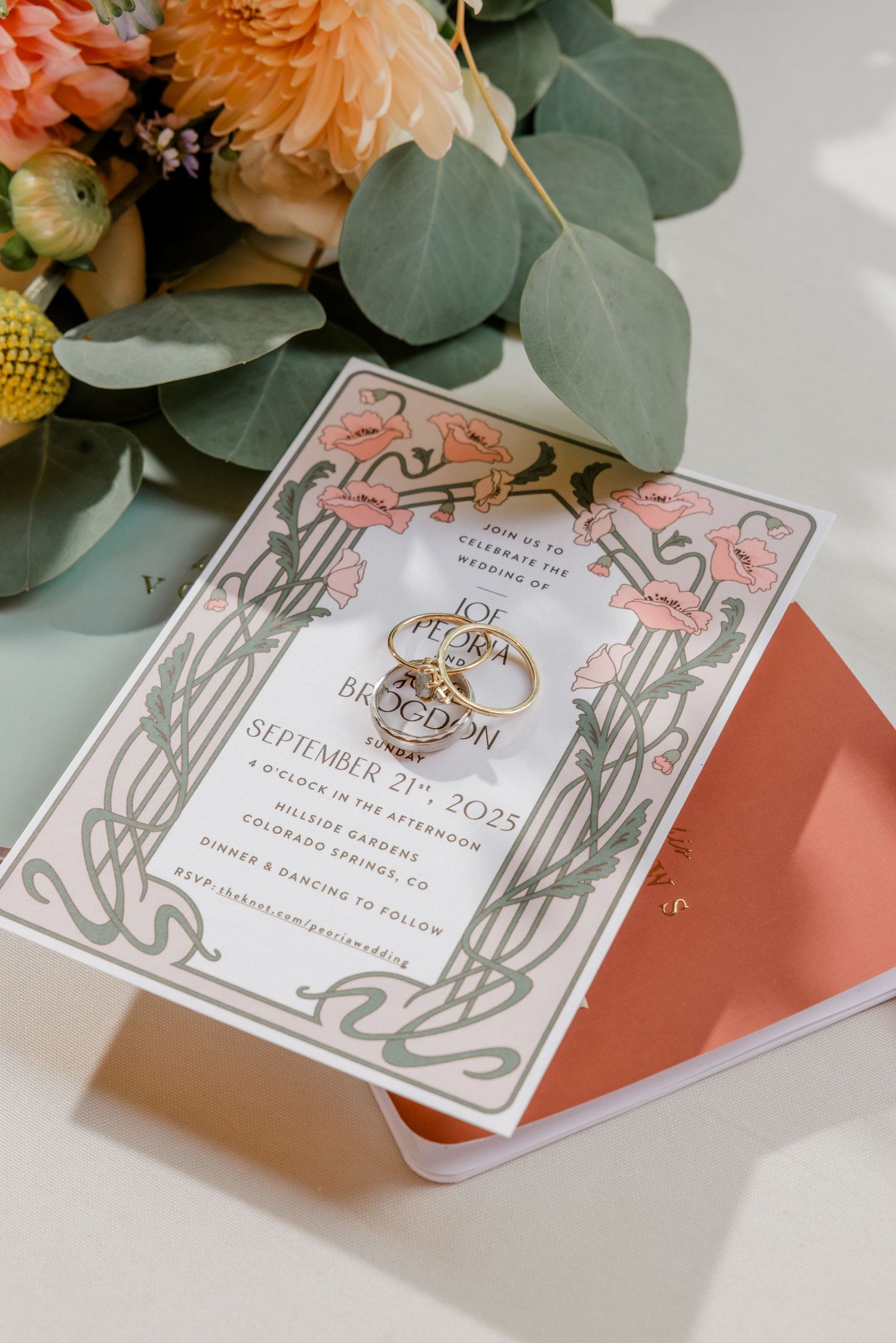 Art nouveau style wedding invitation with coral and gray florals featuring gold wedding rings and peach flowers.