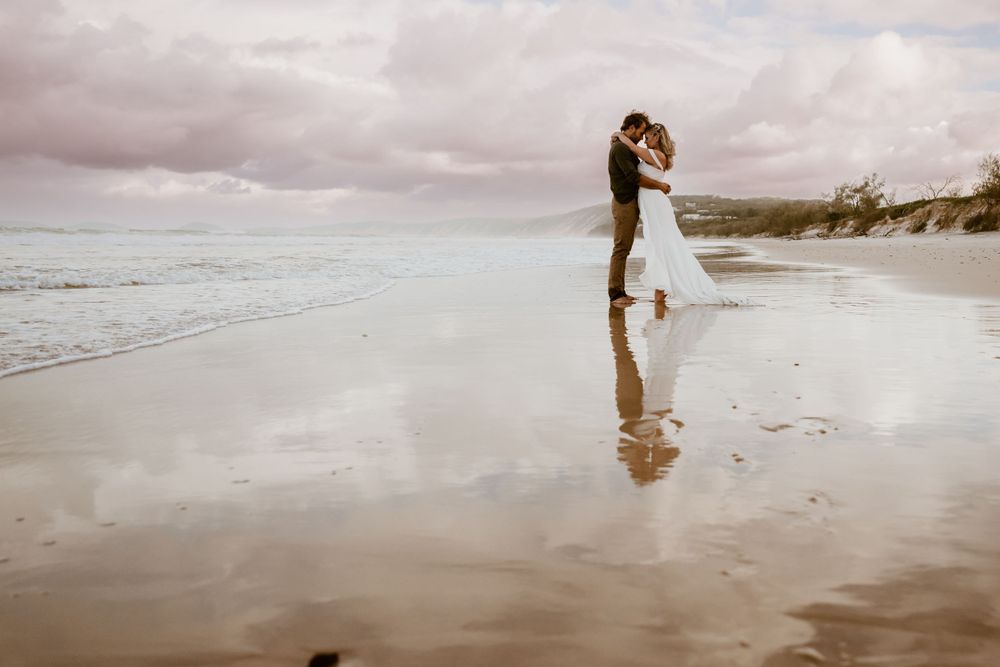 A couple embracing on a misty beach shore with cloudy skies in the background.