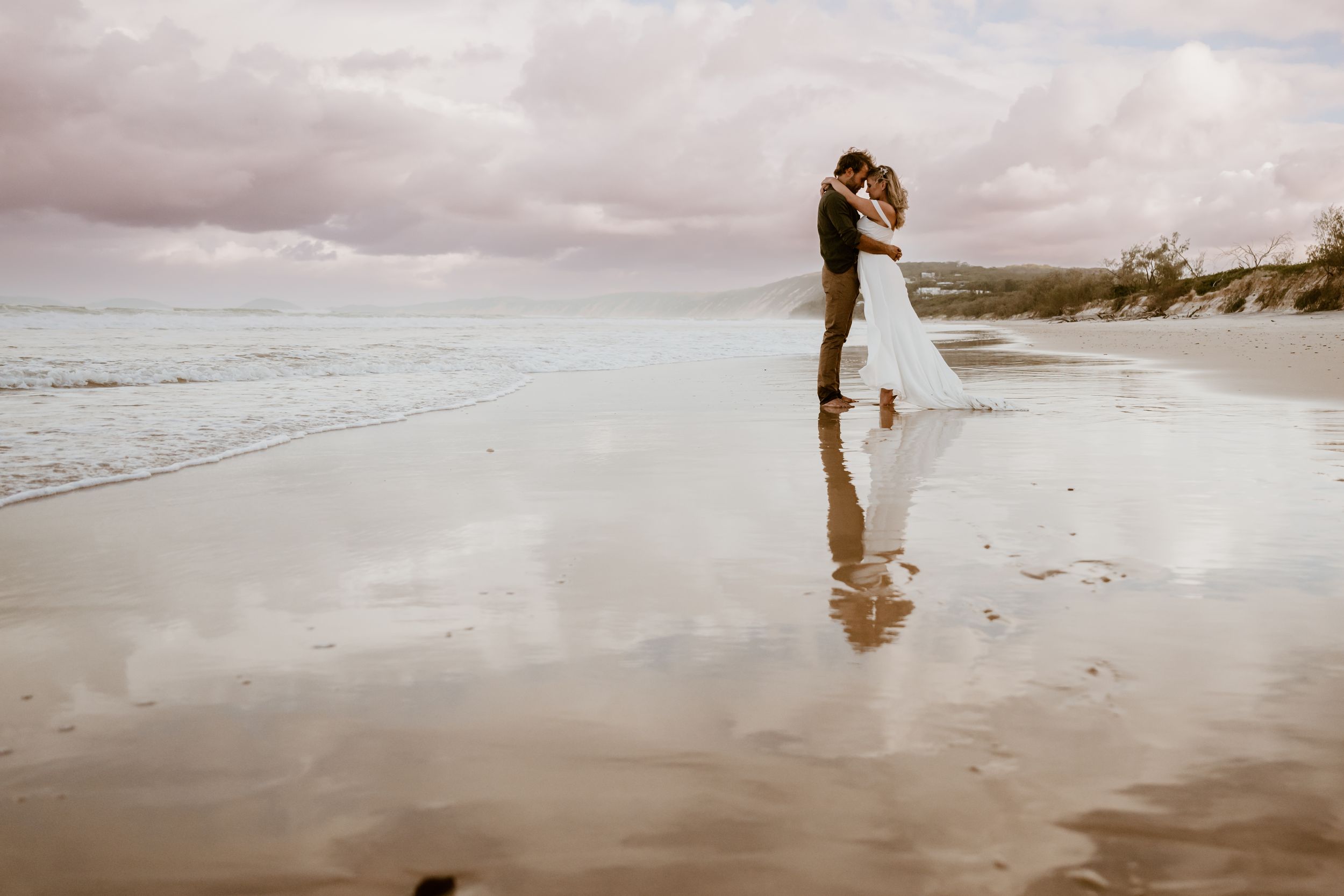 A couple embracing on a misty beach shore with cloudy skies in the background.