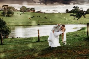 Person in white wedding dress bending down in dramatic pose on green hillside.