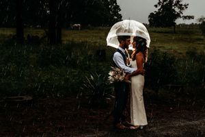 A couple shares an intimate moment under a clear umbrella in the rain during their wedding photoshoot.