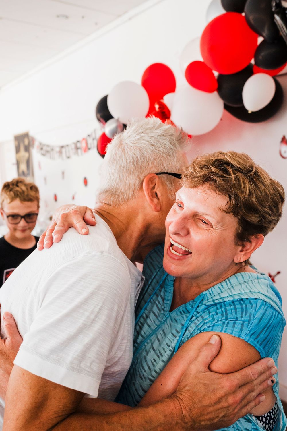 Emotional family moment captured during celebration with red and white balloon backdrop.