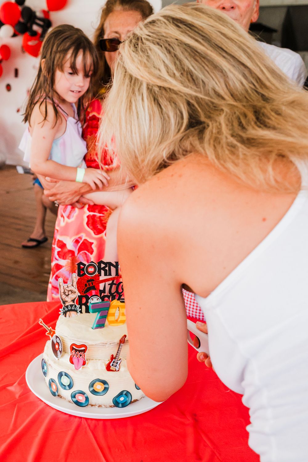 Birthday party scene with red decorations and people gathered around a cake on a table.