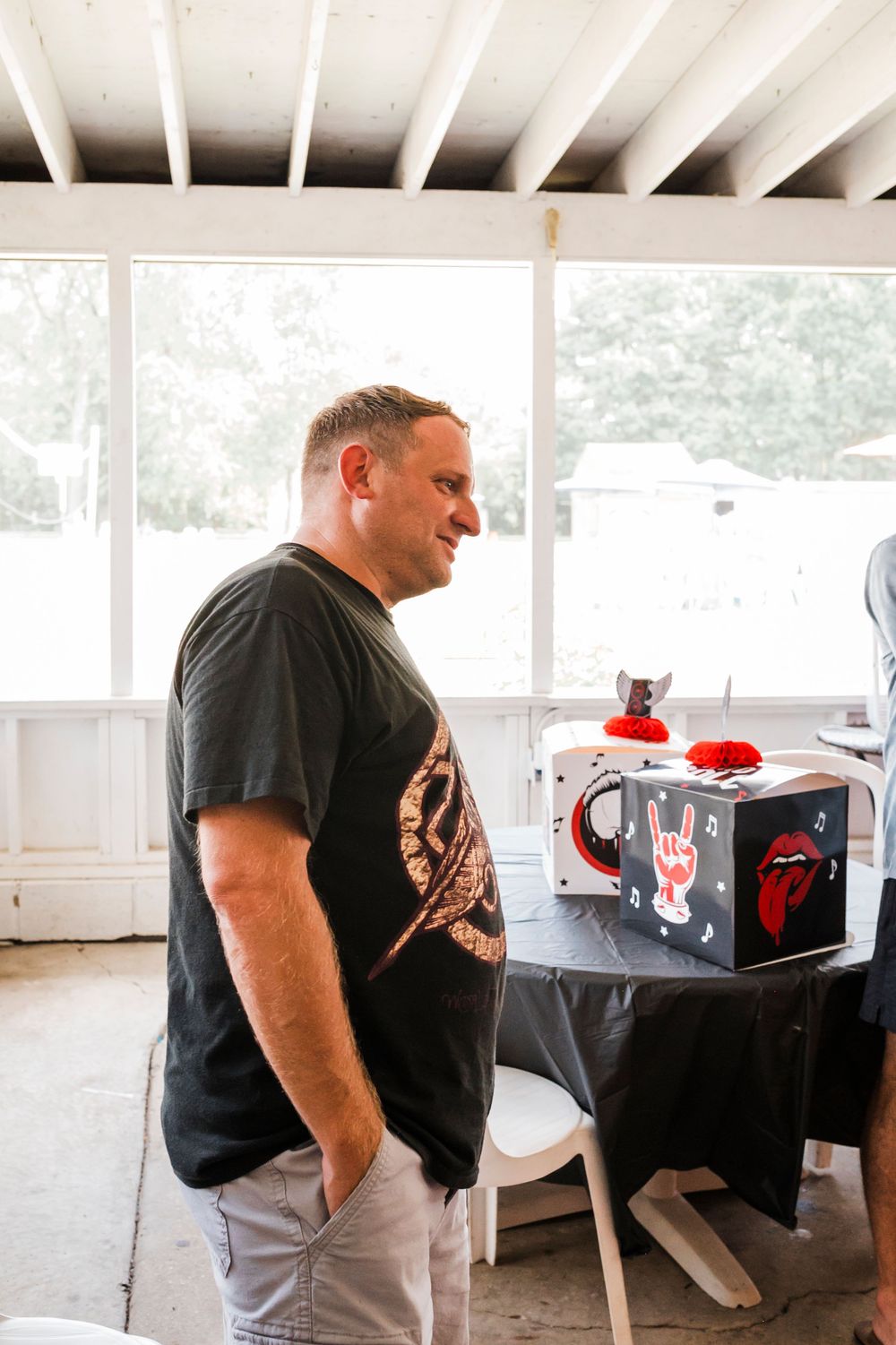 Person in black t-shirt stands near merchandise display table at indoor event.