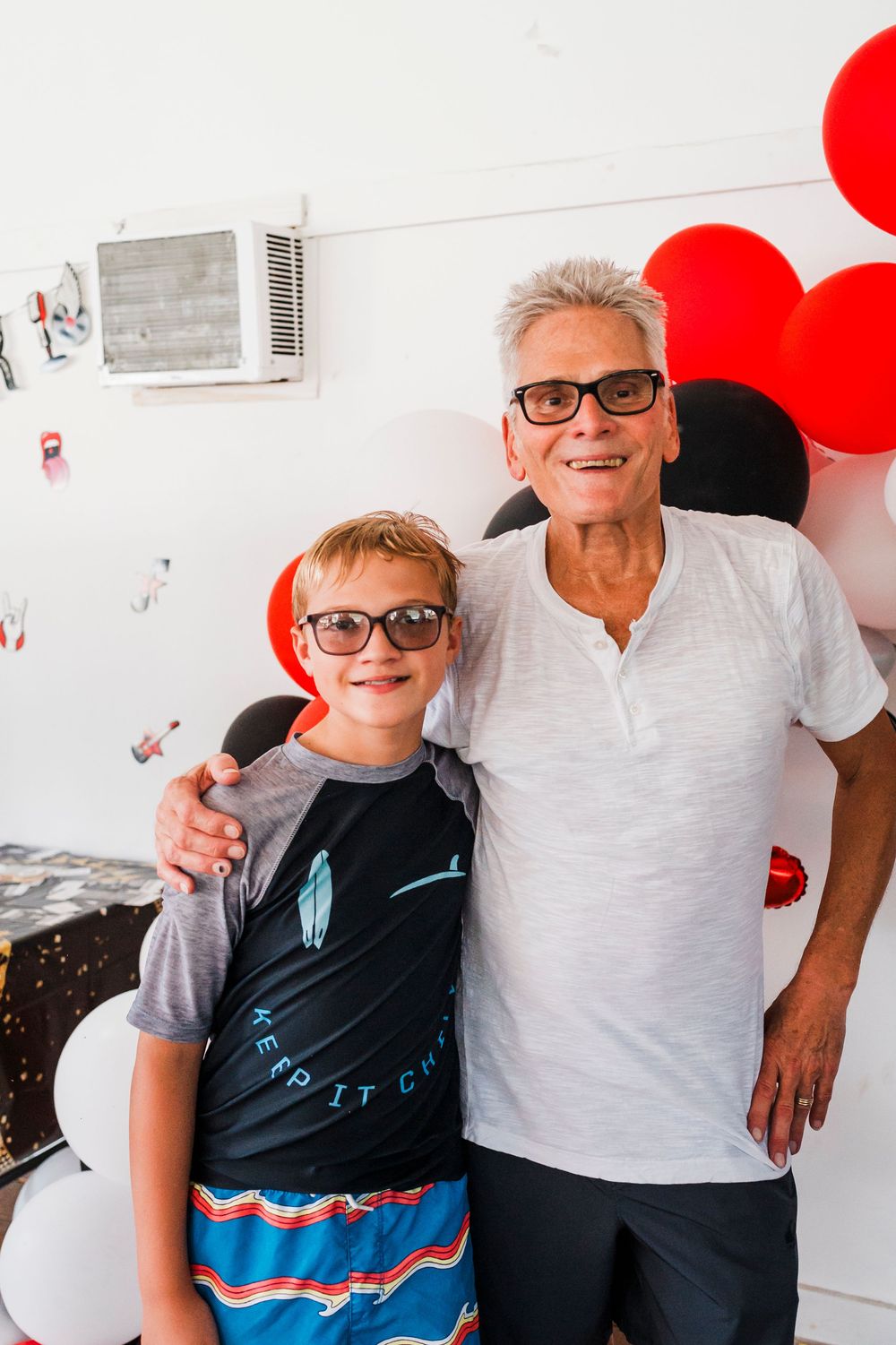 Two people share a joyful moment in front of a balloon-decorated wall.
