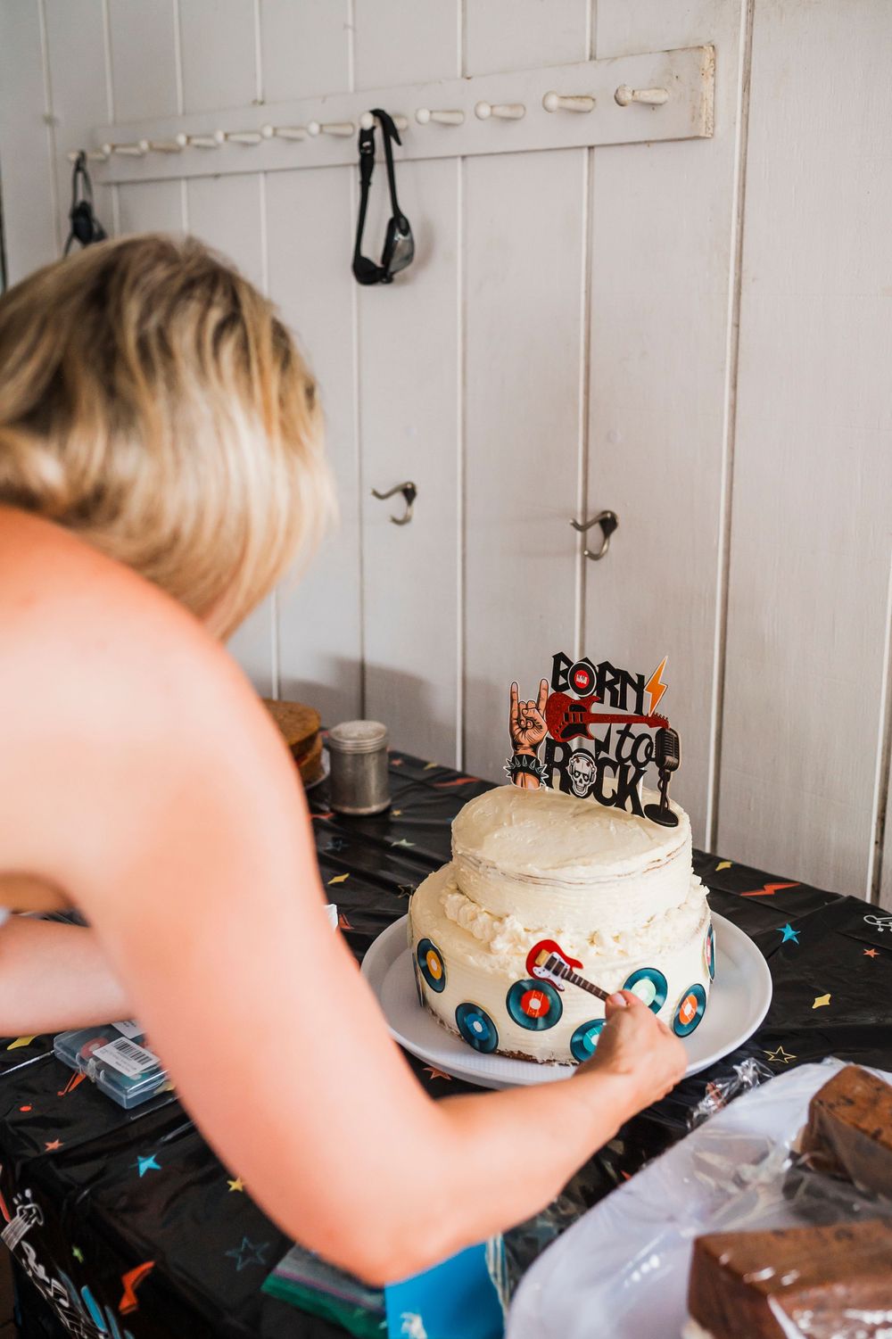A white birthday cake being decorated on a wooden surface with party decorations.