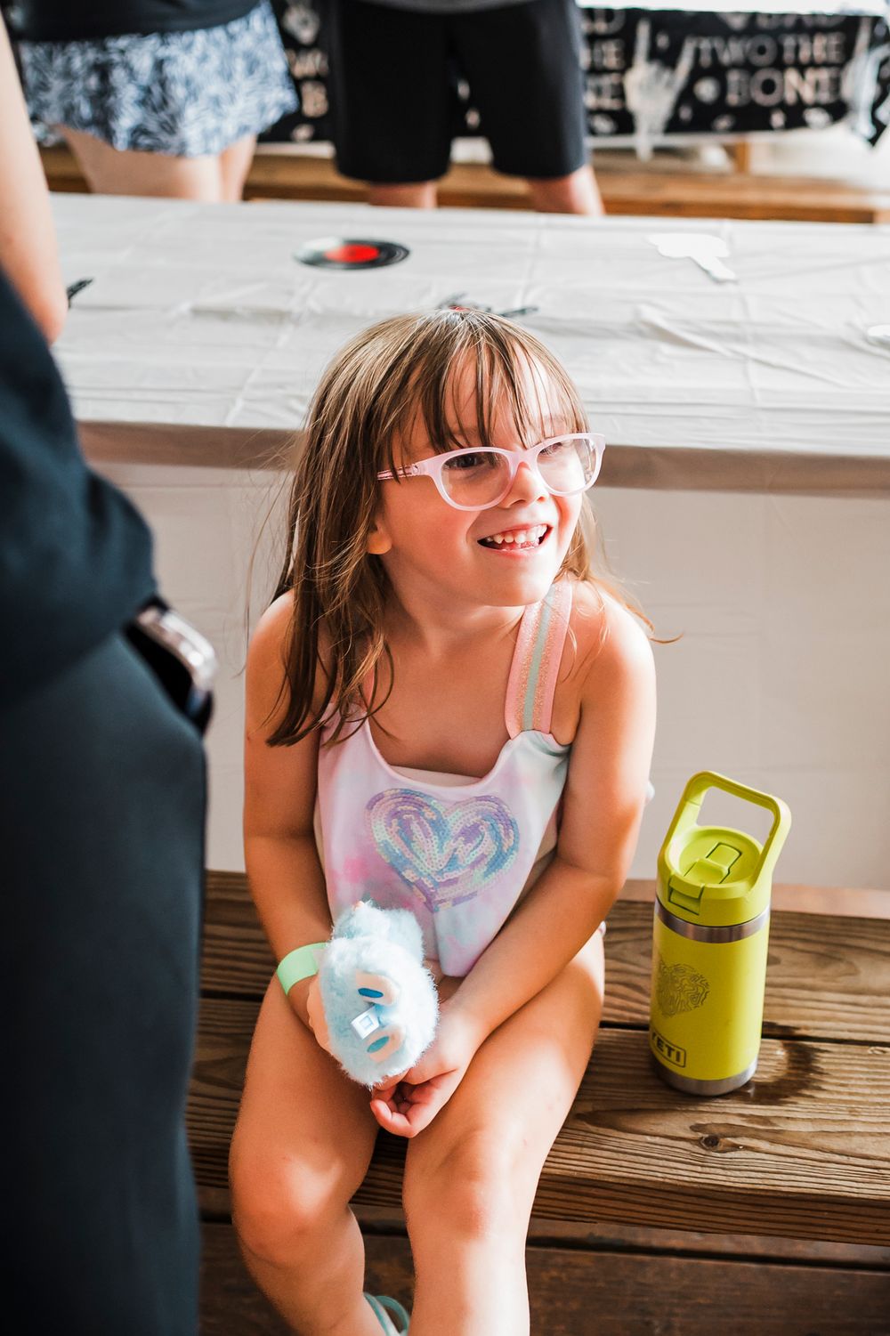 Young person in glasses sits on wooden steps holding a drink container and smiling while enjoying a summer day.