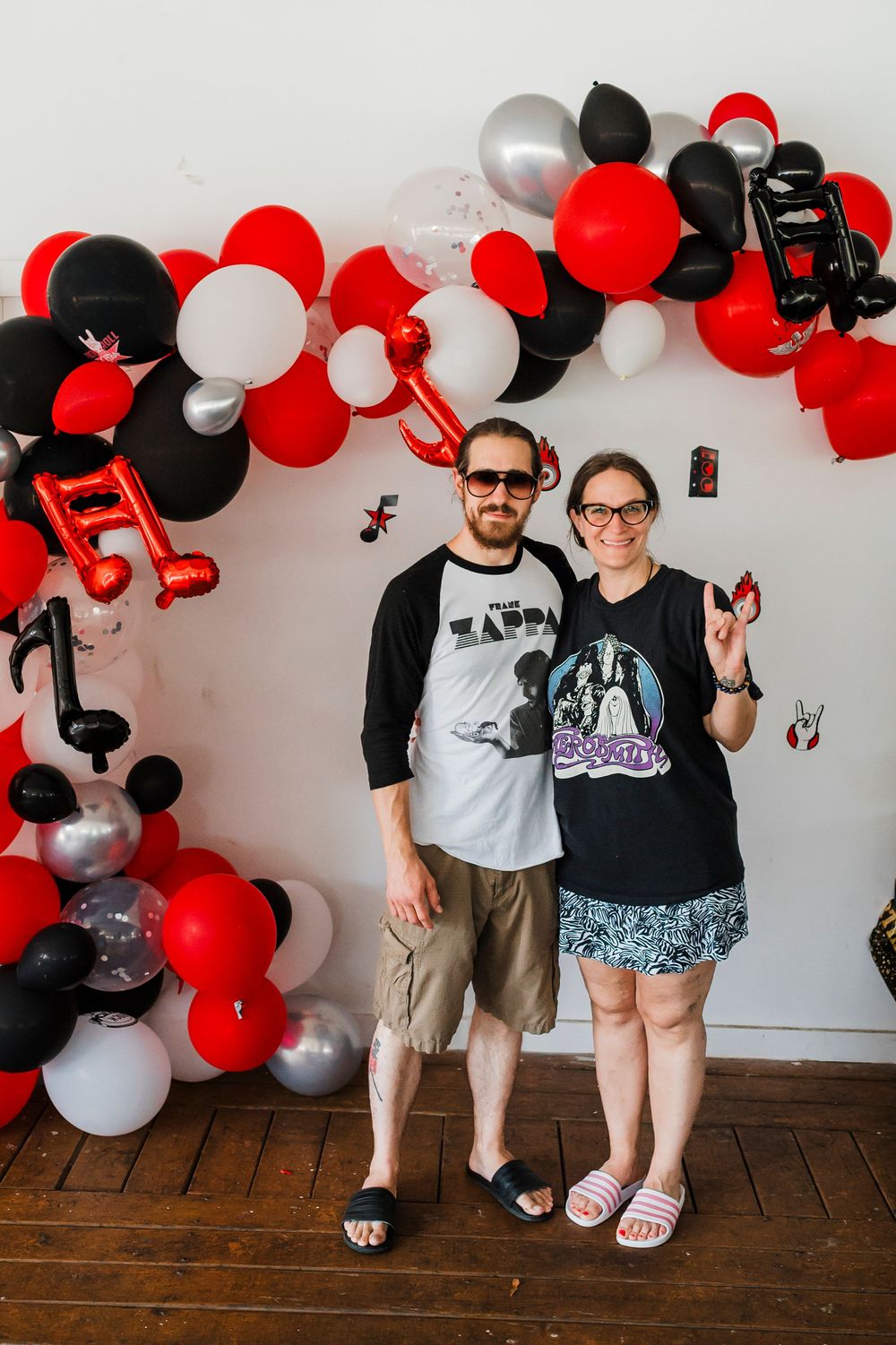 Party decorations with a festive balloon arch in red, black and white colors against a white wall.
