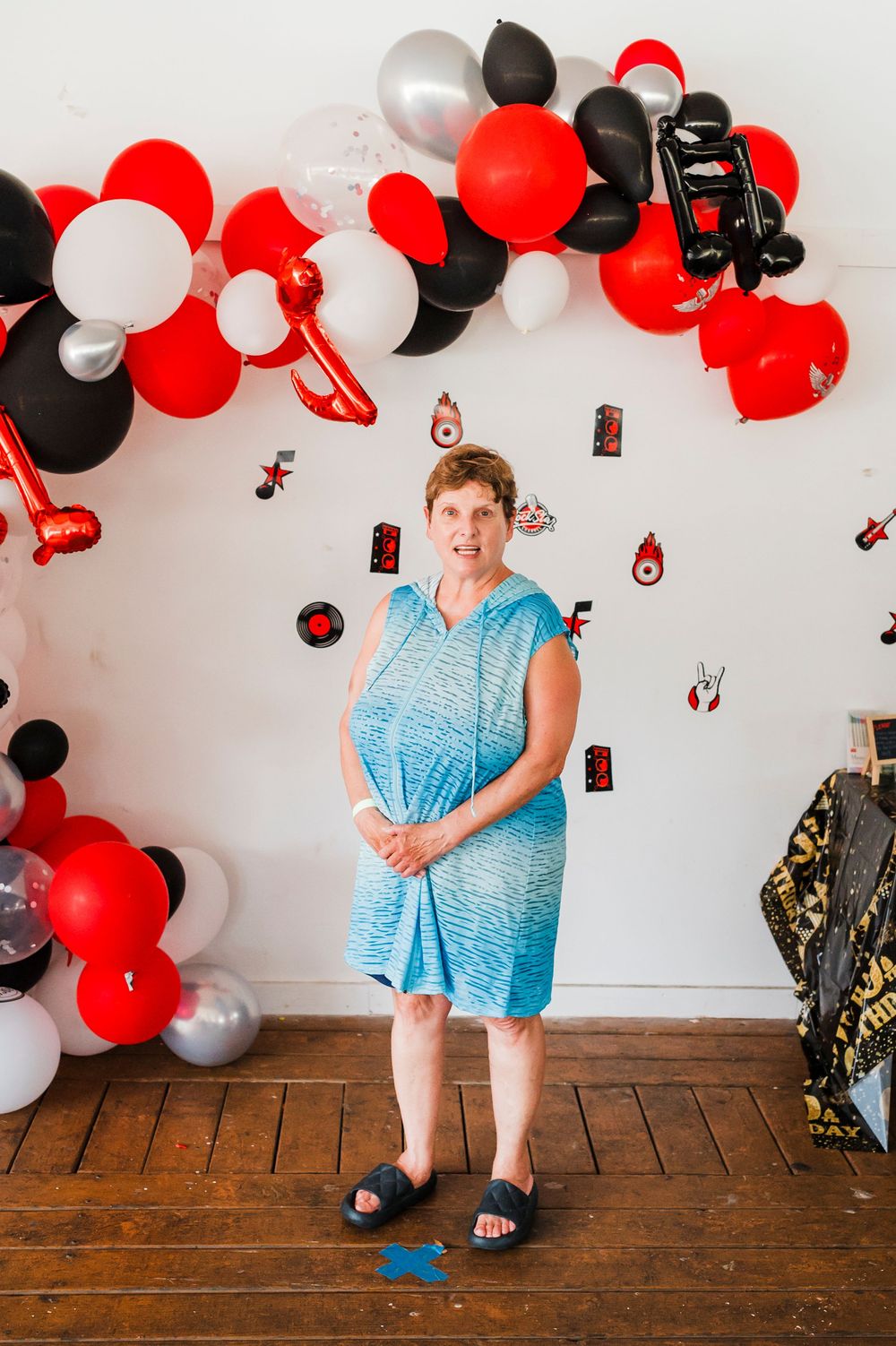 Person in blue dress poses under decorative balloon arch with red and black balloons.