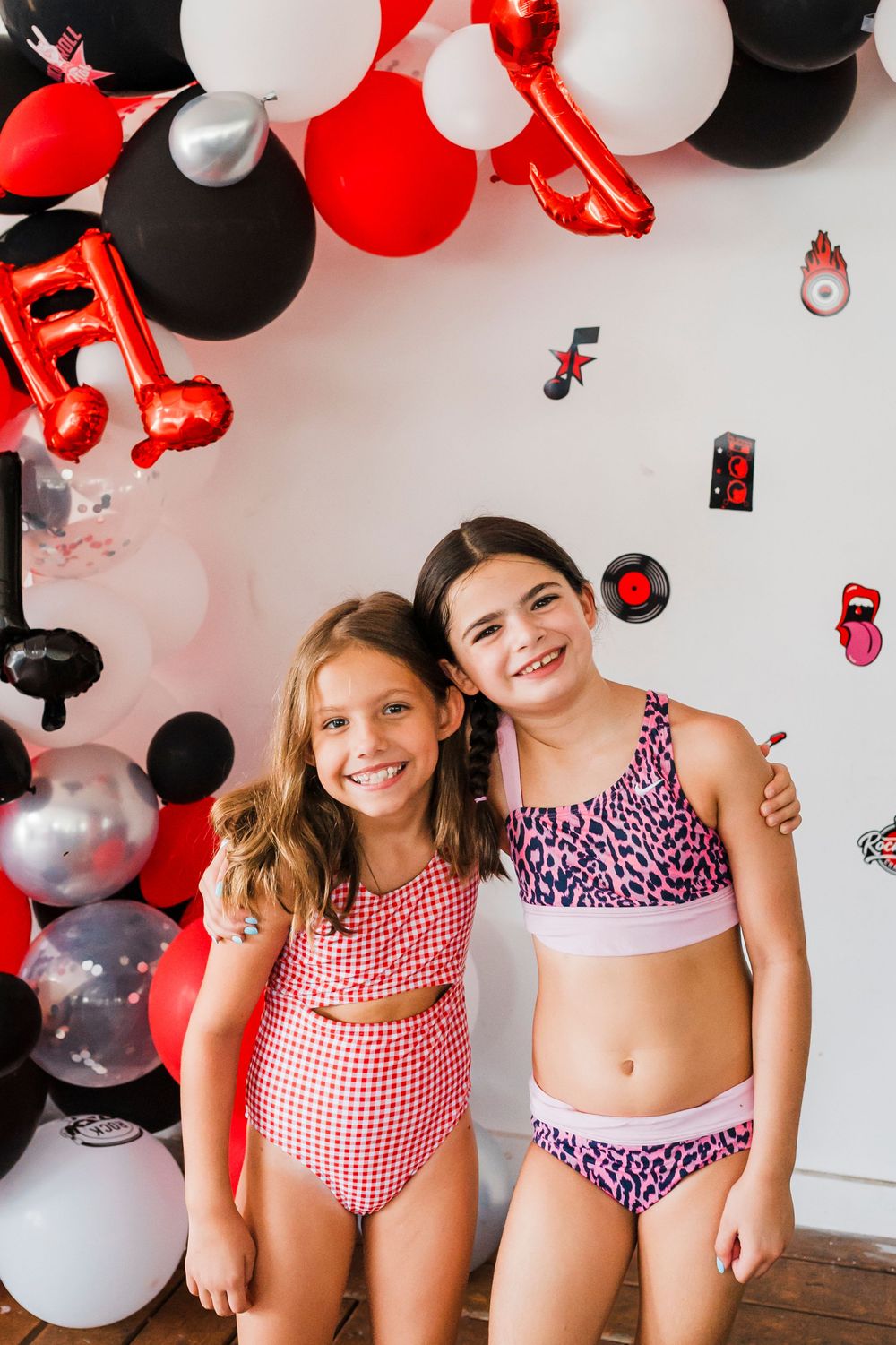 Children in red and white swimsuits pose under festive balloon decorations.