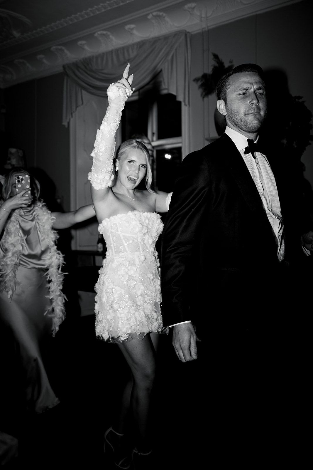 Dancers in vintage 1920s flapper and formal attire perform energetic moves at a party in black and white photography.