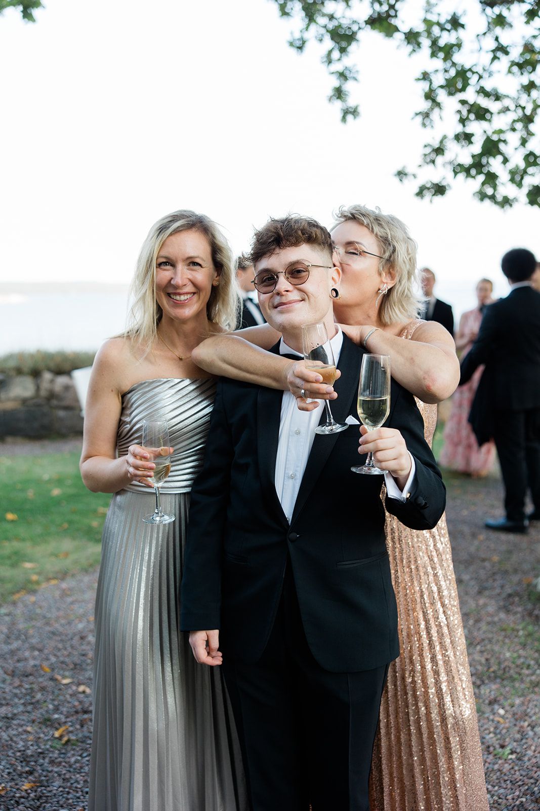 Wedding guests in formal attire share champagne toasts at an outdoor celebration.