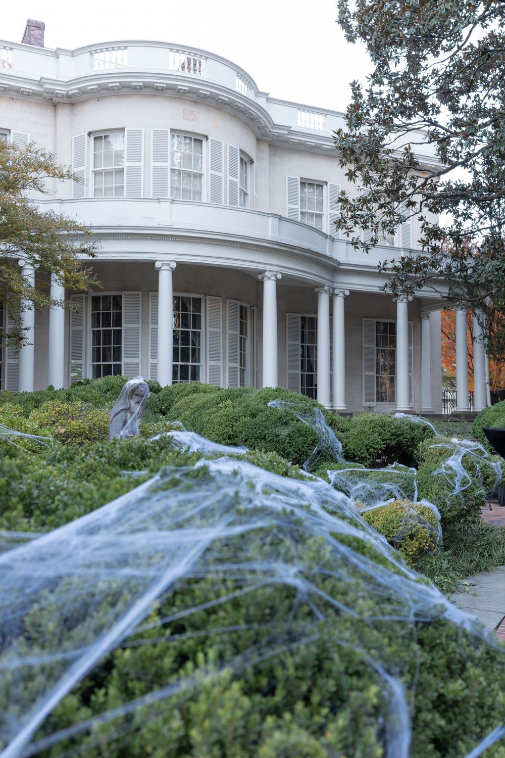 White neoclassical building with columns decorated with spooky spider webs and Halloween decorations in the garden.