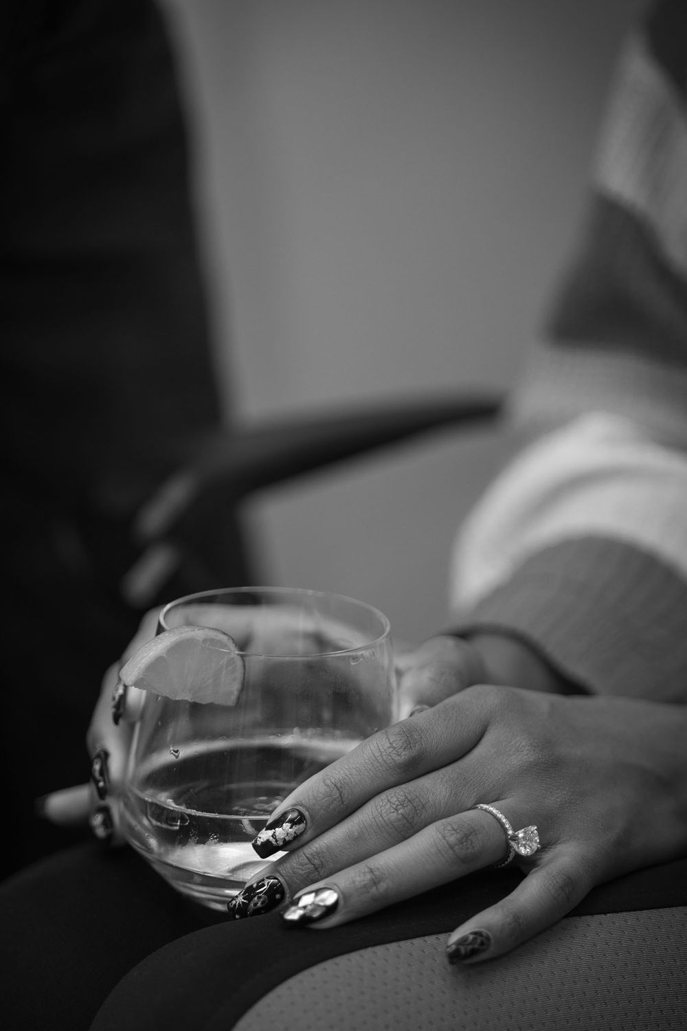 Black and white close-up of hands holding a wine glass with polished nails, creating an elegant and moody atmosphere.