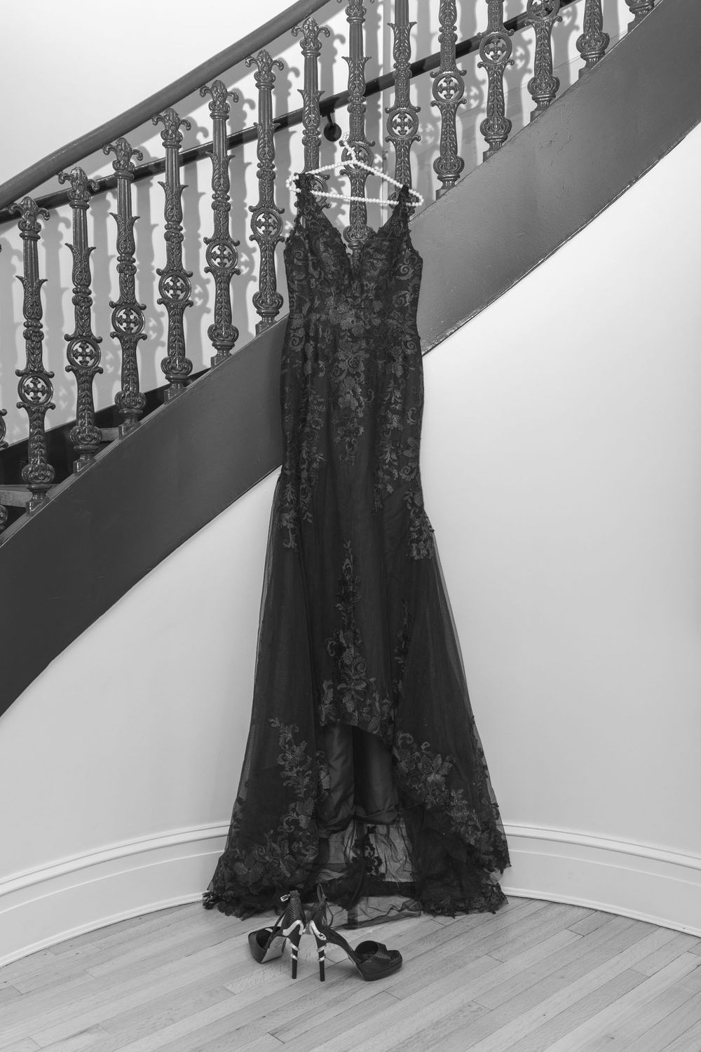 A black lace evening gown displayed in a dramatic series of poses against a white wall with wooden staircase railing.