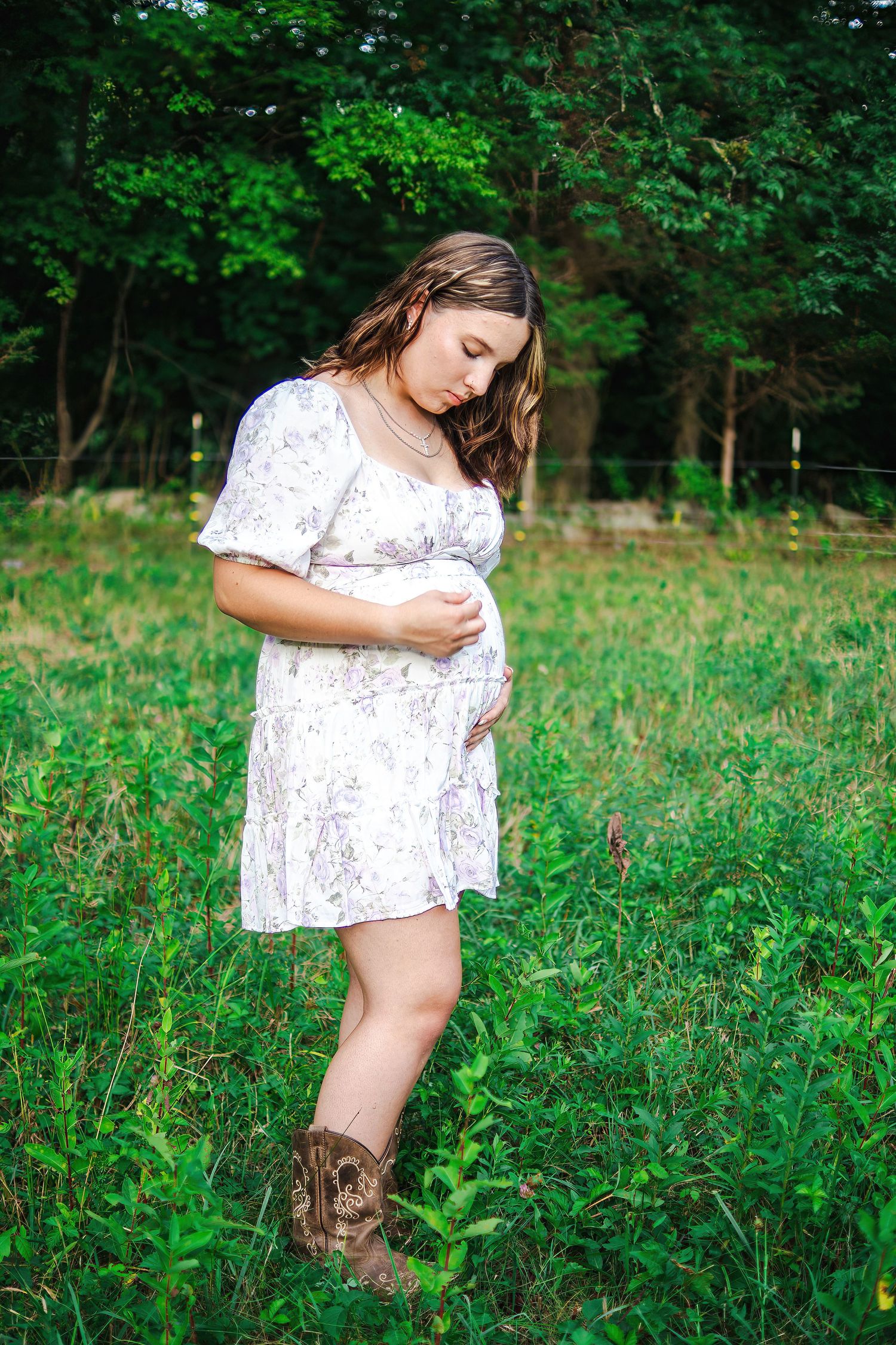 Person in a floral dress and boots poses in a green summer field.