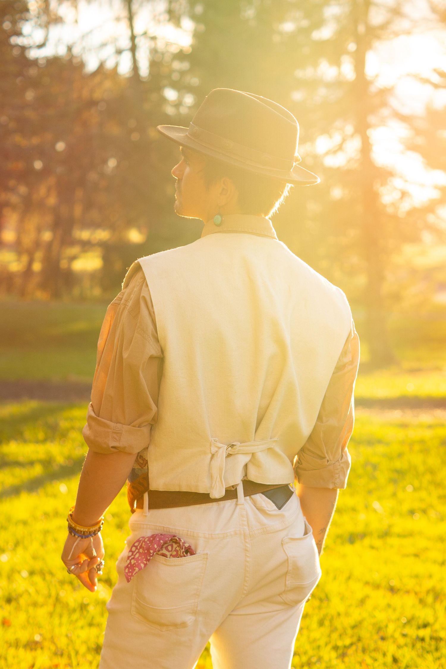 Silhouette of person in western wear walking through sunlit field at golden hour.