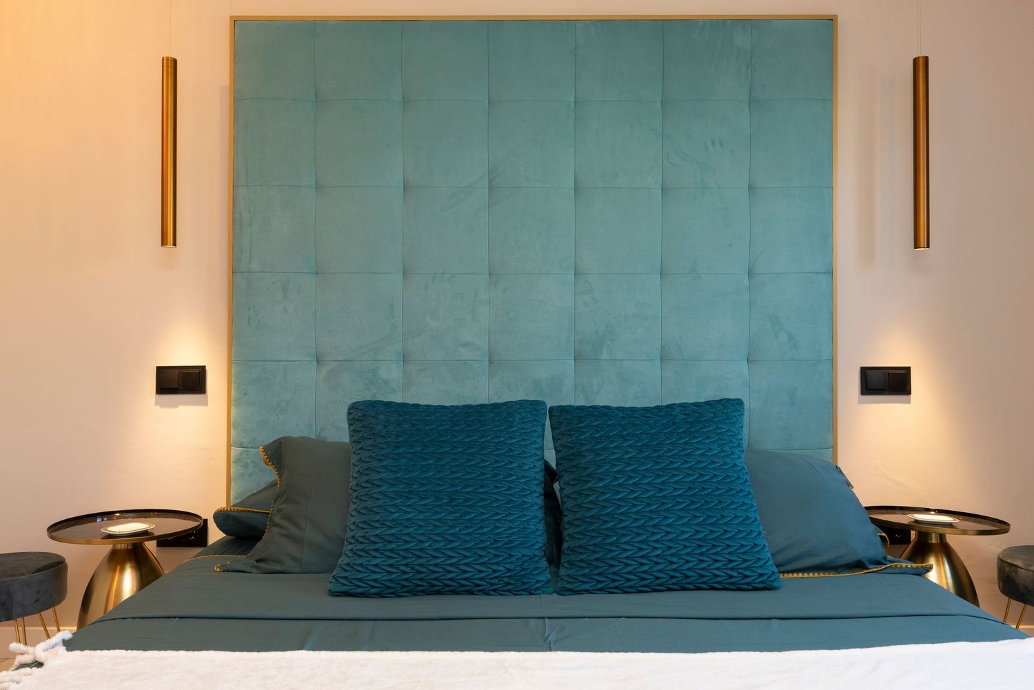 Modern bedroom interior with white bedding, wooden accents, and natural light streaming through vertical windows.