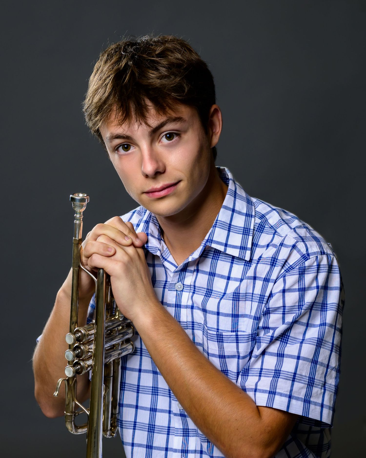 Person in blue checkered shirt holding up a trumpet in various poses against dark background.