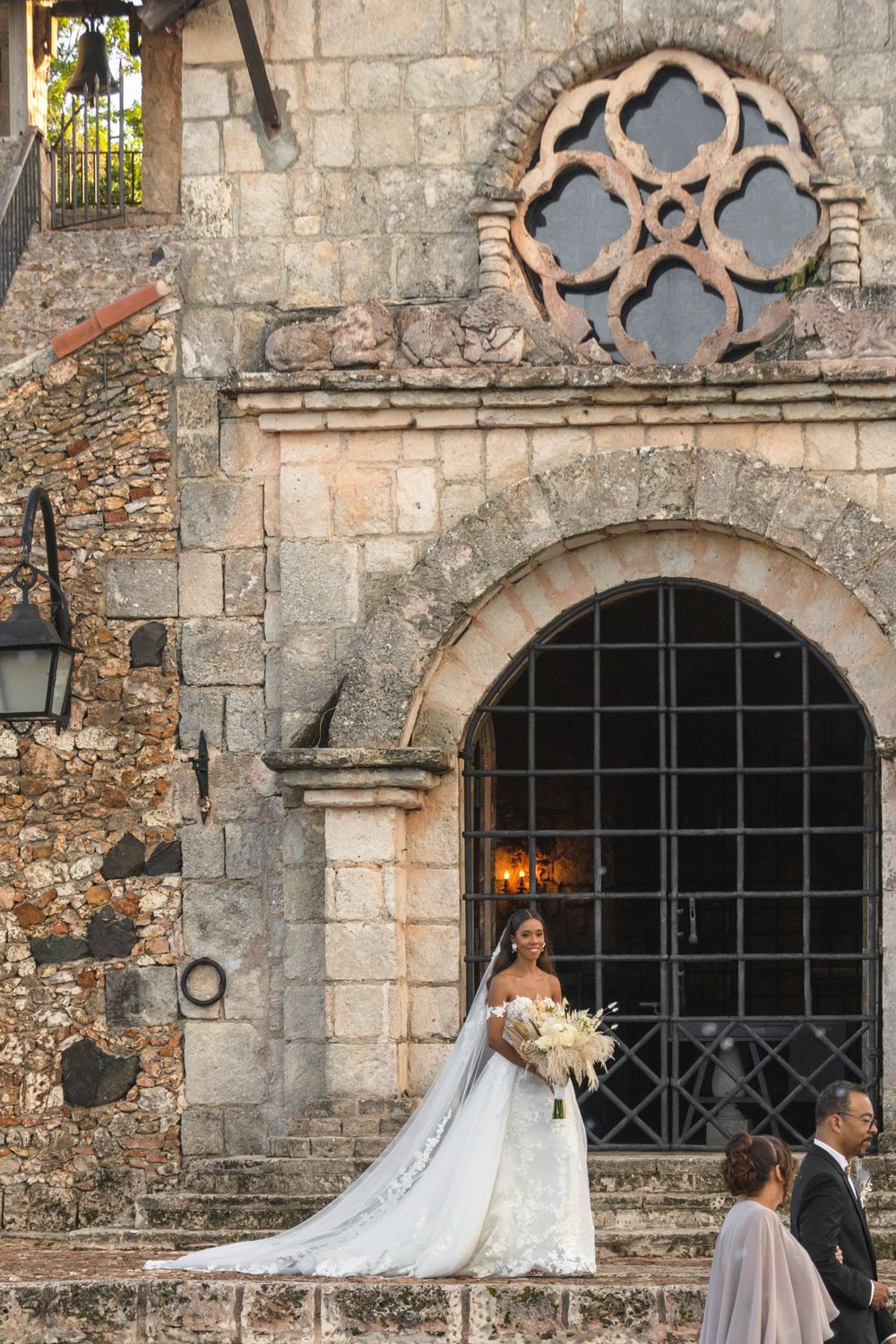 A wedding couple poses in front of a historic stone church with gothic architectural details.