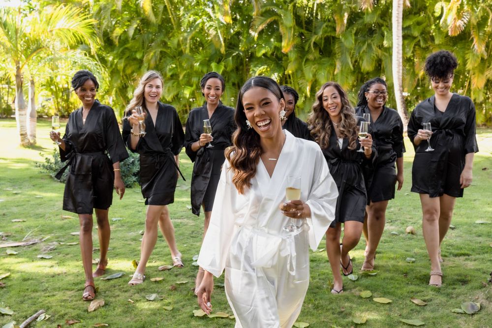 A group wearing black and white formal attire walks together on a grassy lawn during a sunny outdoor gathering.