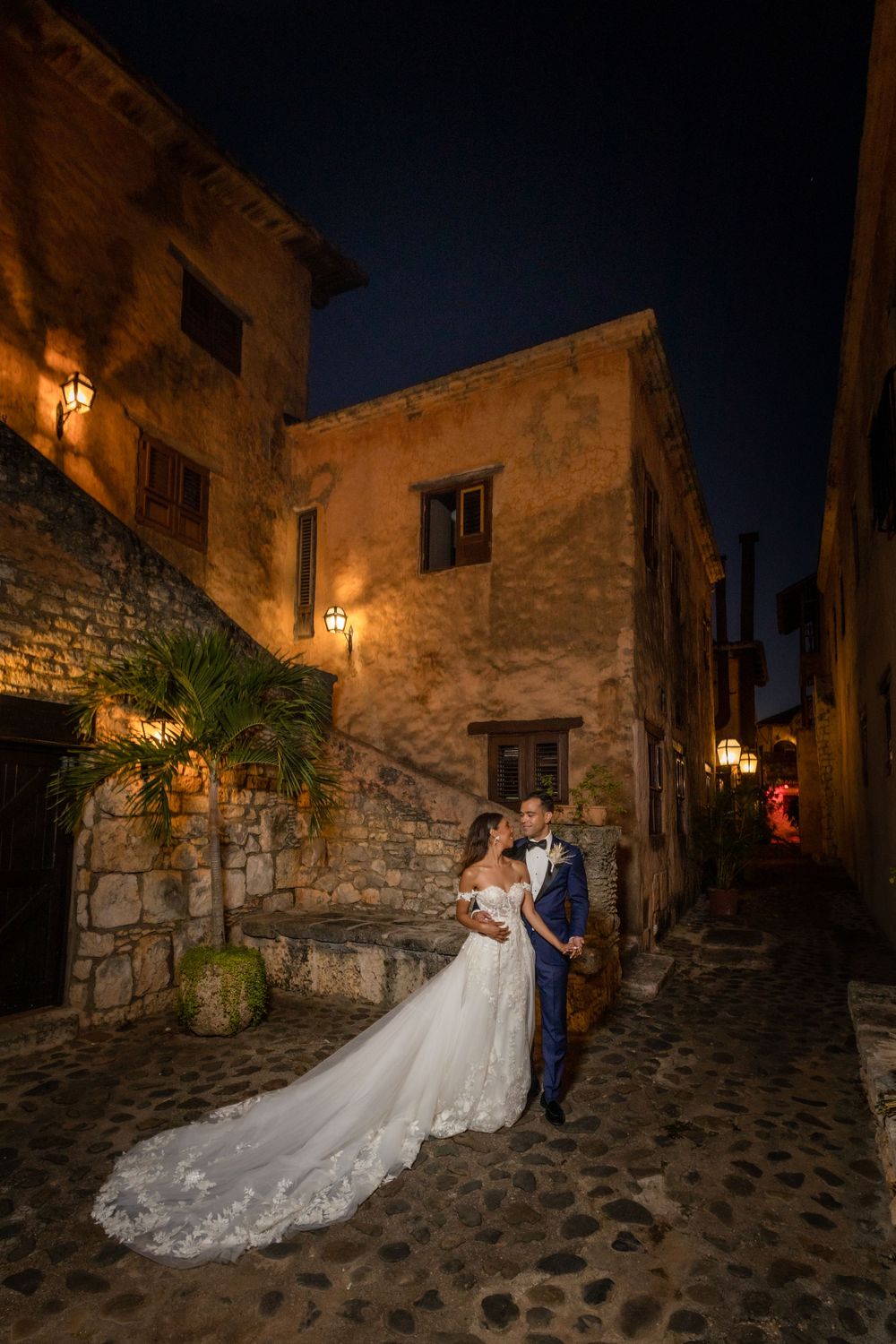 A nighttime wedding portrait in a cobblestone alley lit by warm glowing lanterns.