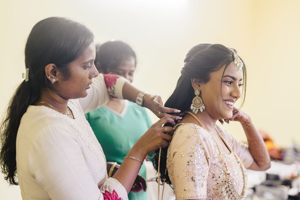 A bride getting ready for her wedding with traditional Indian bridal makeup being applied in a soft-lit room.